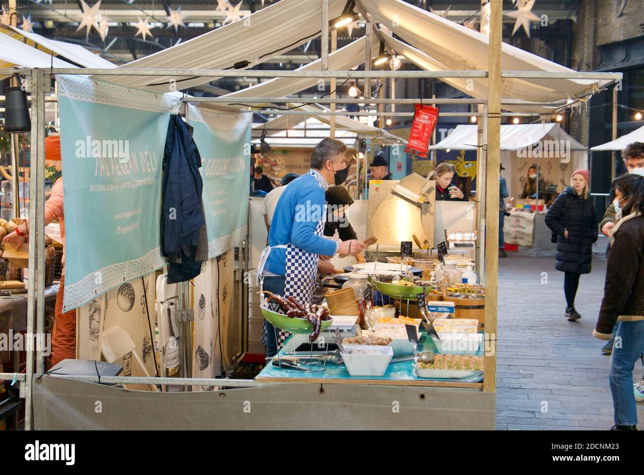 Mann mit Gesichtsmaske serviert türkische Süßigkeiten und Wraps auf einem Canopy Food Market in Coal Drops Yard, Kings Cross, London. Stockfoto