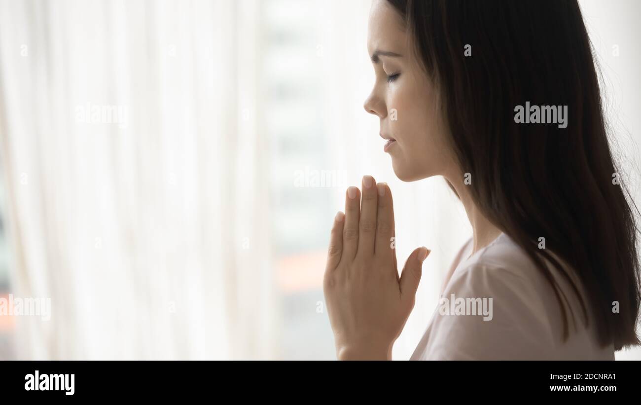 Konzentrierte religiöse junge Frau, die Gott betet und Handflächen miteinander verbindet Stockfoto