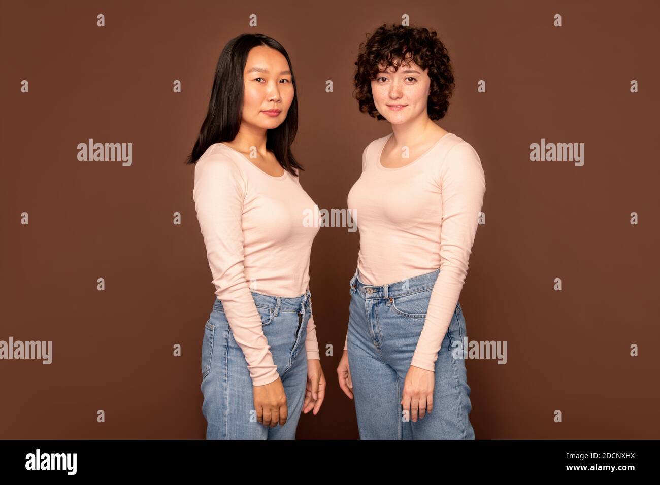Zwei junge Frauen in weißen Pullovern und blauen Jeans stehen Nah beieinander Stockfoto