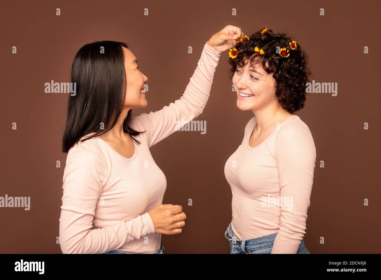 Eine von zwei jungen interkulturellen Frauen, die kleine Blumen hineinstecken Haare ihrer Freundin Stockfoto