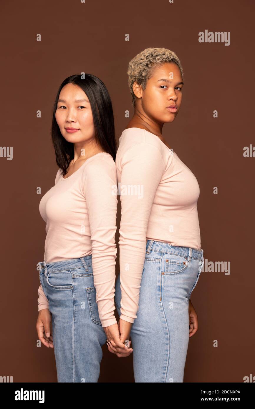 Seitenansicht von zwei jungen interkulturellen Frauen in weißen Pullovern Wenn du dich ansiehst Stockfoto