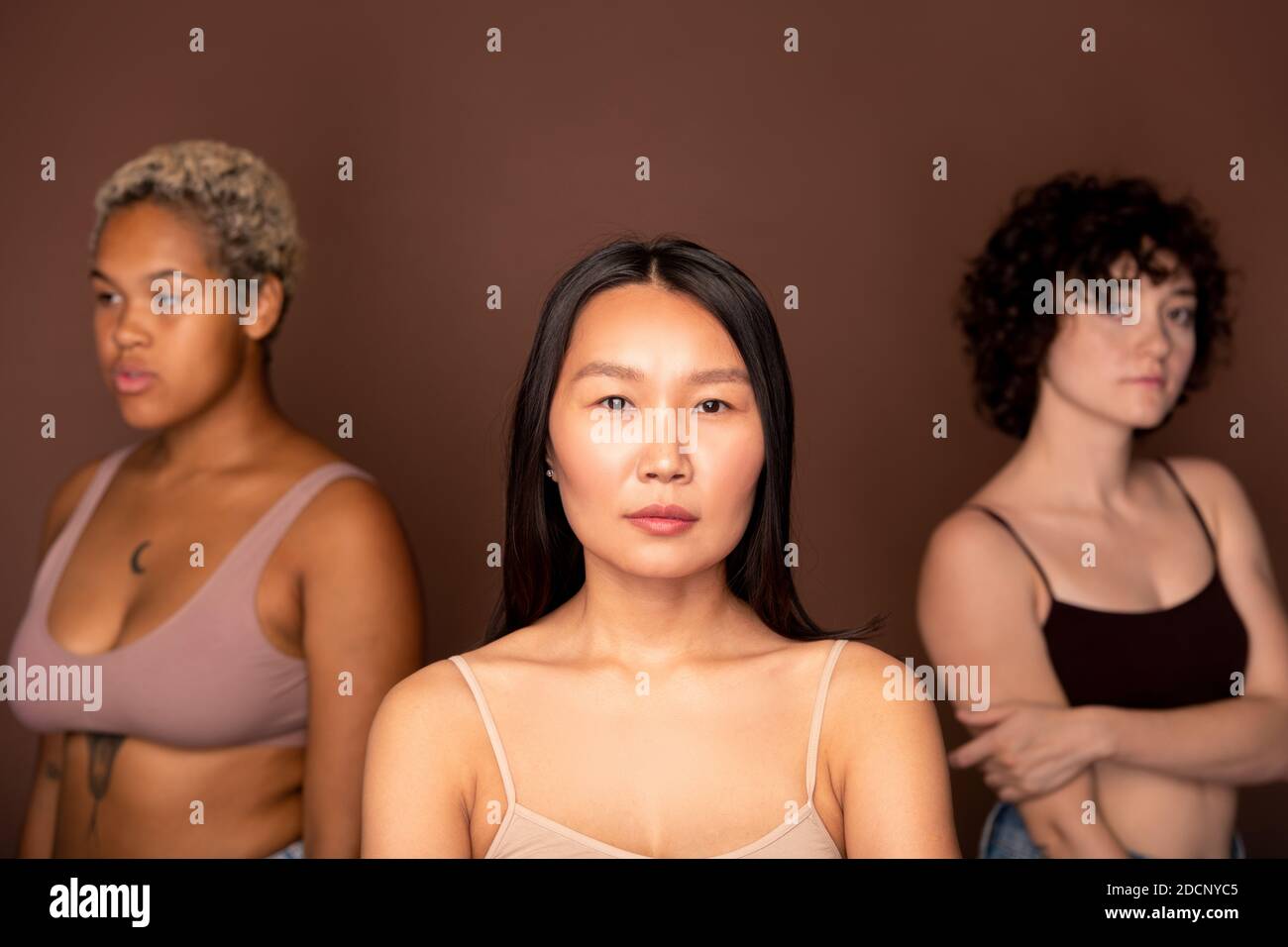 Junge seriöse asiatische Frau in beige Tanktop stehen gegen zwei Andere Frauen Stockfoto