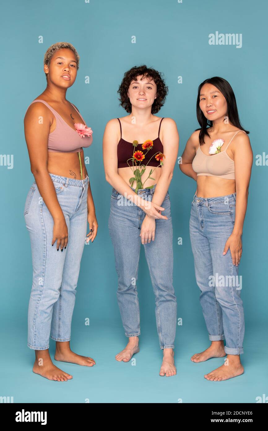 Drei junge hübsche Frauen mit schönen frischen Blumen in Tanktops Und Jeans Stockfoto