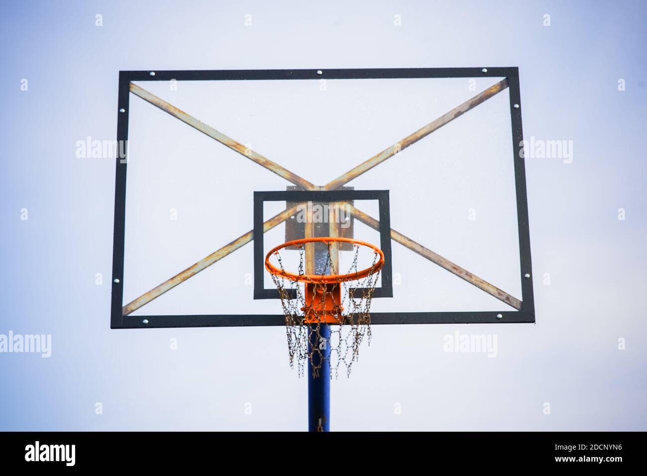 Basketballkorb mit transparentem Brett und Ketten statt Netz Gegen den hellblauen klaren Himmel am Nachmittag ab Einen vorderen unteren Winkel Stockfoto
