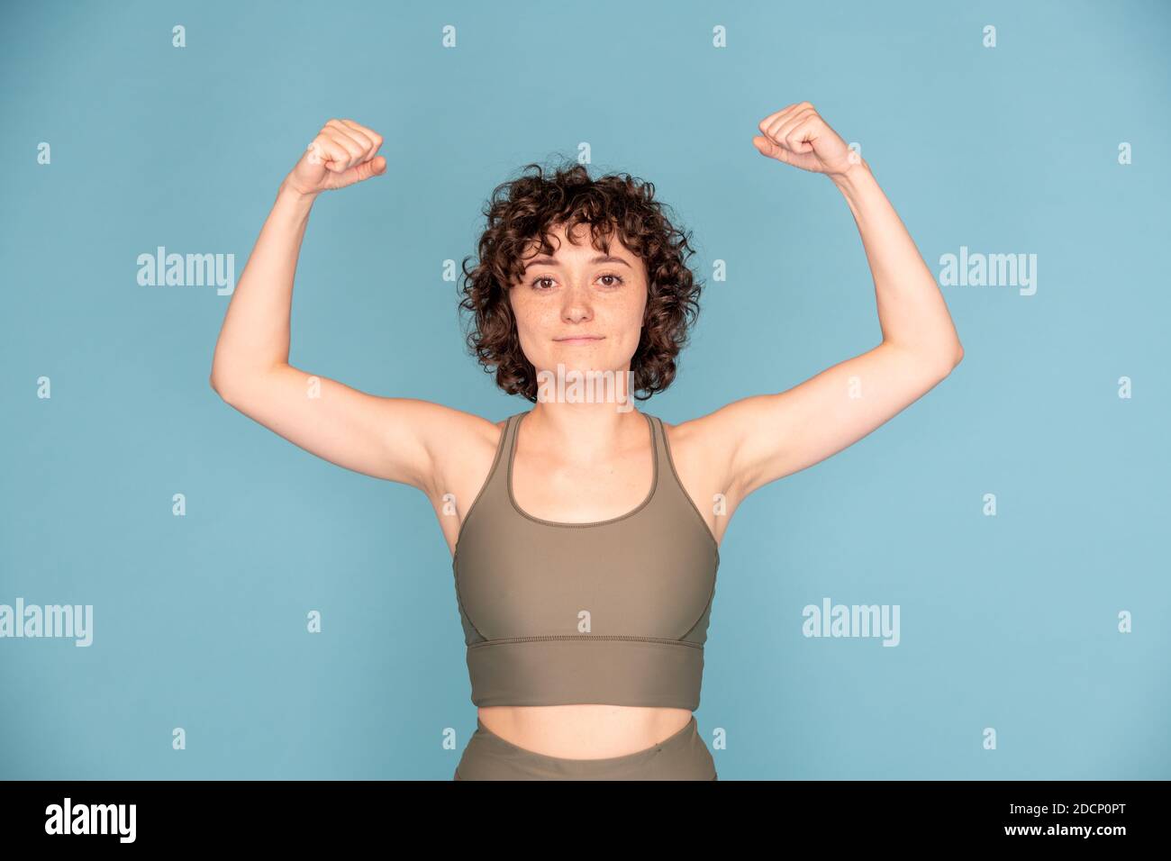 Fröhliche junge Sportlerin in grau Trainingsanzug zeigt Kraft und Training Stockfoto