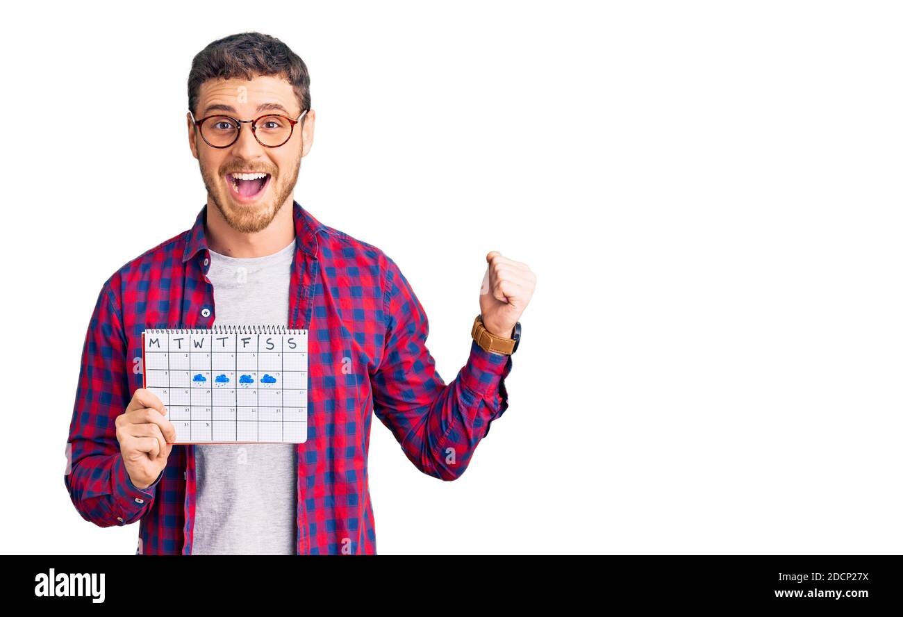 Schöner junger Mann mit Bär hält Reisekalender schreiend stolz, feiert Sieg und Erfolg sehr aufgeregt mit erhobenen Armen Stockfoto