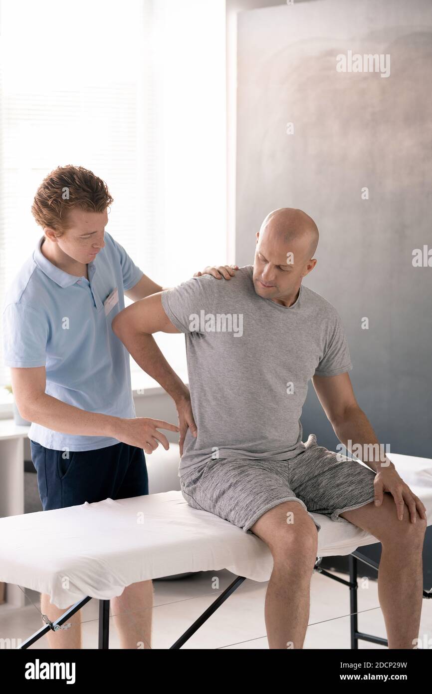 Bald reifer Mann mit Schmerzen im Rücken sitzend auf Medizinische Couch in Kliniken Stockfoto