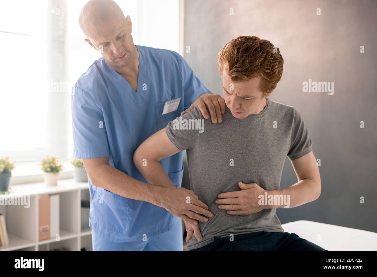 Kranker Mann, der dem Arzt zeigt, wo es weh tut und rechts berührt Seines Rückens Stockfoto