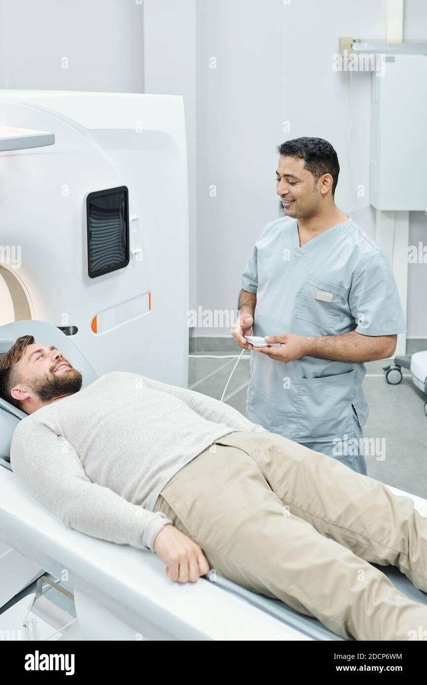 Glücklicher gemischter männlicher Arzt in medizinischer Uniform und lächelnd bärtig Patient Stockfoto