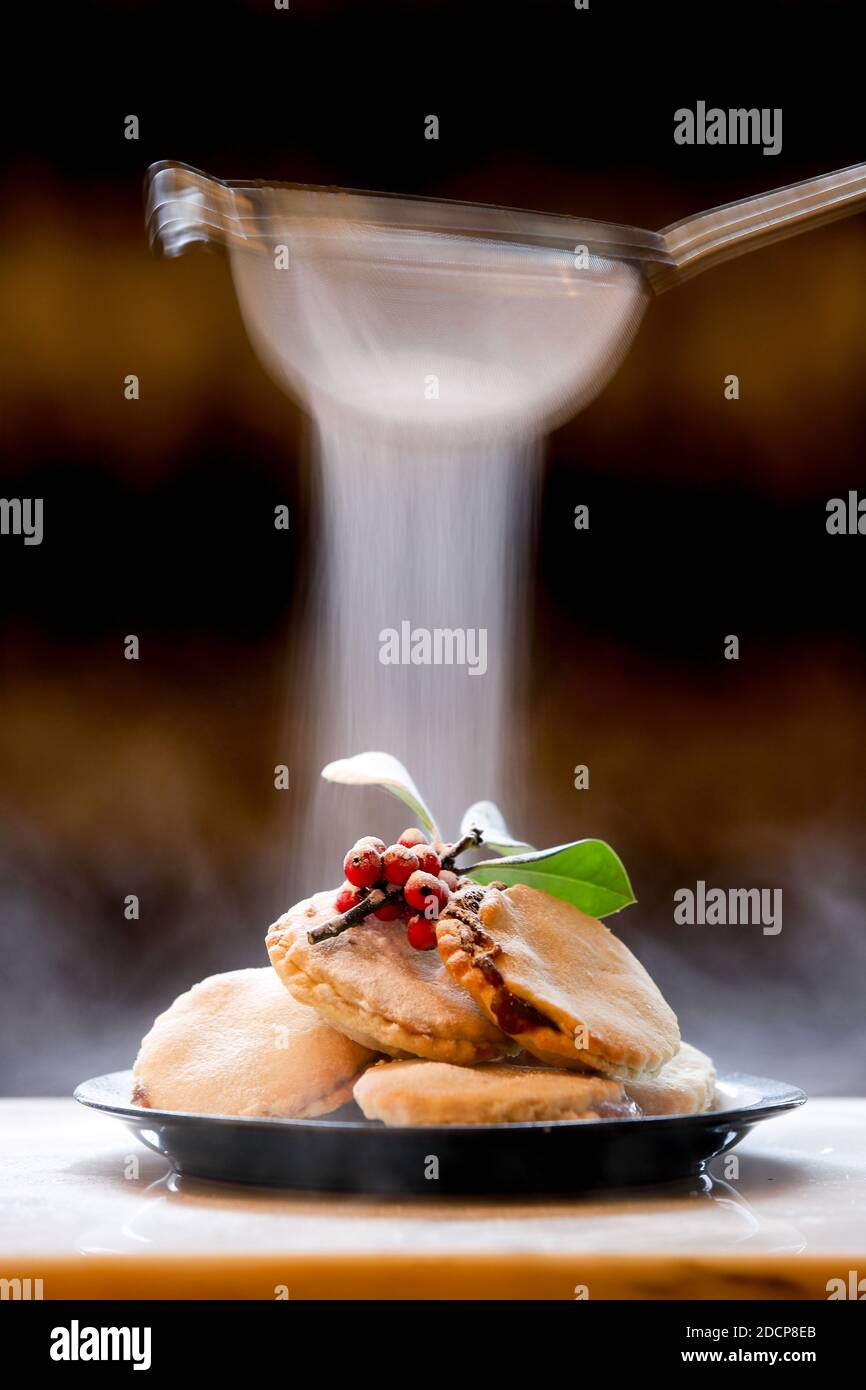 Hausgemachte Mince Pies mit einem Zweig von Stechpalme dekoriert und eine leichte Staubbildung von Puderzucker gegeben. Stockfoto