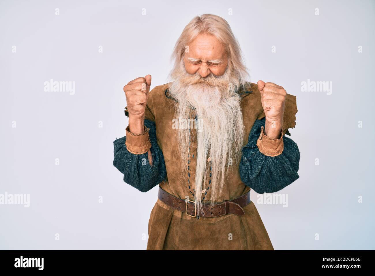 Alter älterer Mann mit grauen Haaren und langem Bart tragen viking Tracht begeistert für den Erfolg mit erhobenen Armen und Augen geschlossen, um victo zu feiern Stockfoto