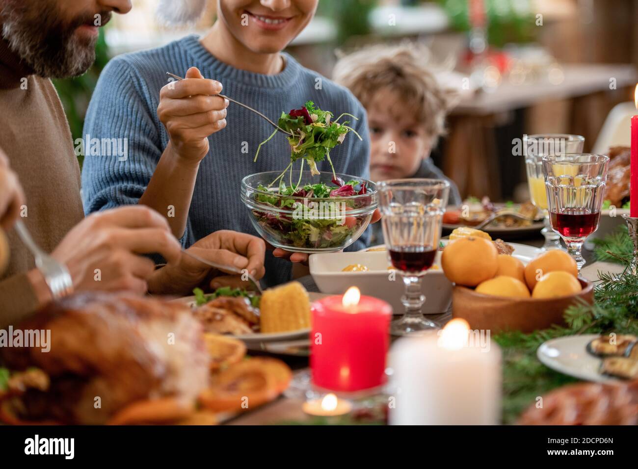 Junge lächelnde Frau, die Gemüsesalat aus der Schüssel auf den Teller legt Ihres Mannes Stockfoto