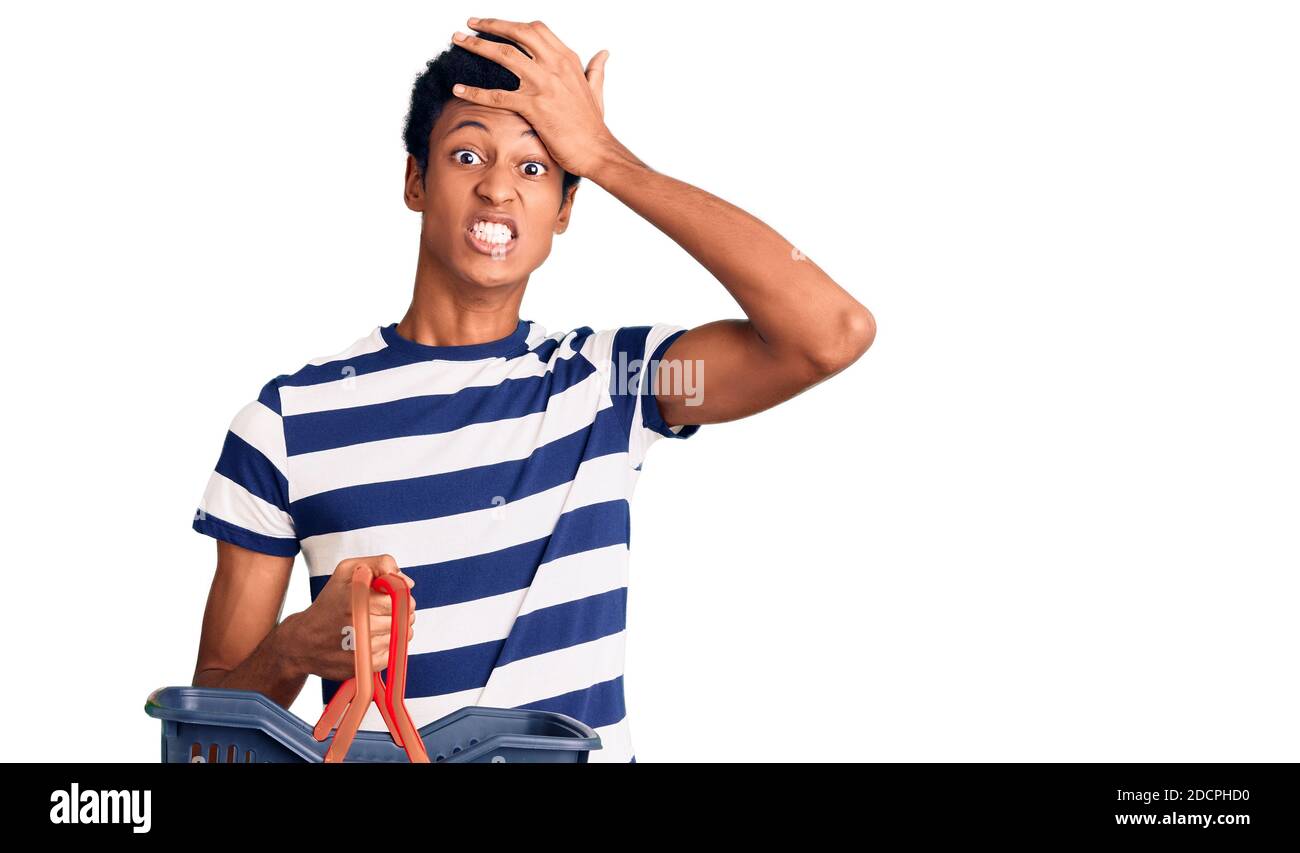 Junger afroamerikanischer Mann, der Supermarkt-Einkaufskorb hält, gestresst und frustriert mit der Hand auf dem Kopf, überrascht und wütend ins Gesicht Stockfoto