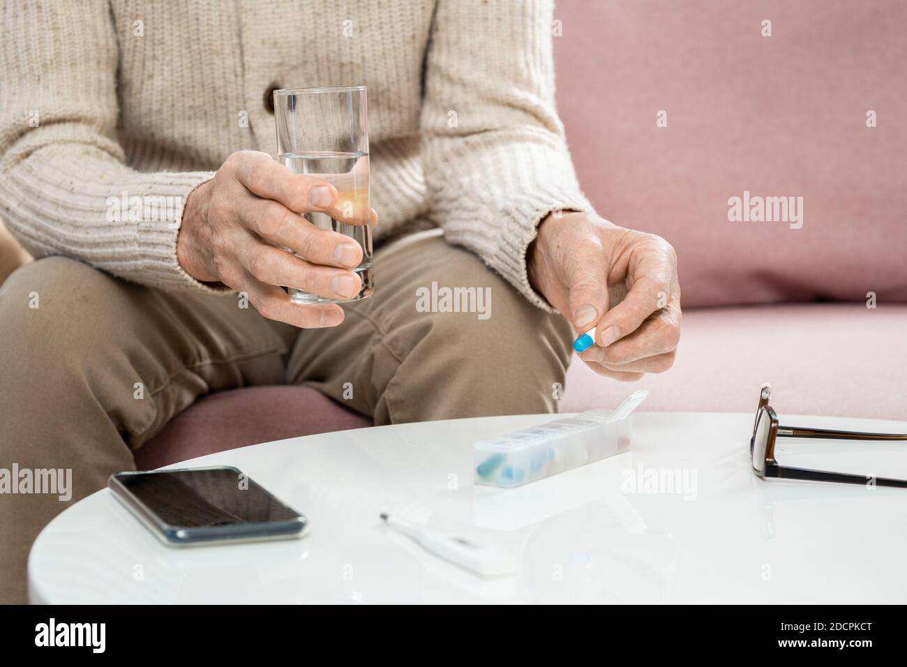 Hände von älteren Mann in Casualwear halten Pille und Glas Von Wasser über dem Tisch Stockfoto