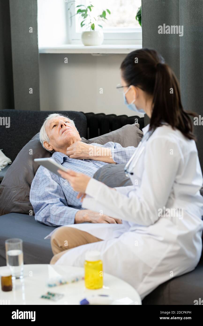 Kranker älterer Mann, der seine Kehle berührte, während er eine Ärztin zeigte Wo es weh tut Stockfoto
