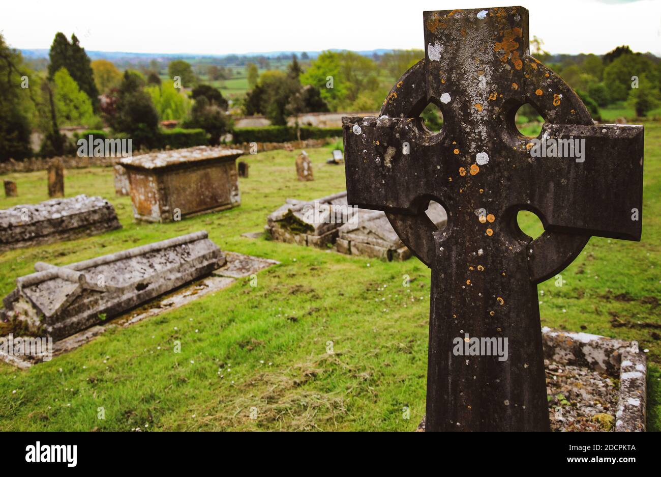 Nahaufnahme eines keltischen Kreuzes in einer Gemeinde der Alten Welt friedhof in St. Michael & All Angels Kirche mit Blick auf ein Hügelige Landschaft der englischen Landschaft Stockfoto