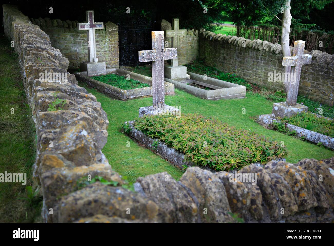 Gut gepflegter alter versunkener Friedhof mit steinernen Kreuzen, die mit Mauern umgeben sind Trockener Stein und scharfe Kapselsteine im historischen Stil in St. Michael & All Angels Kirche in Stockfoto