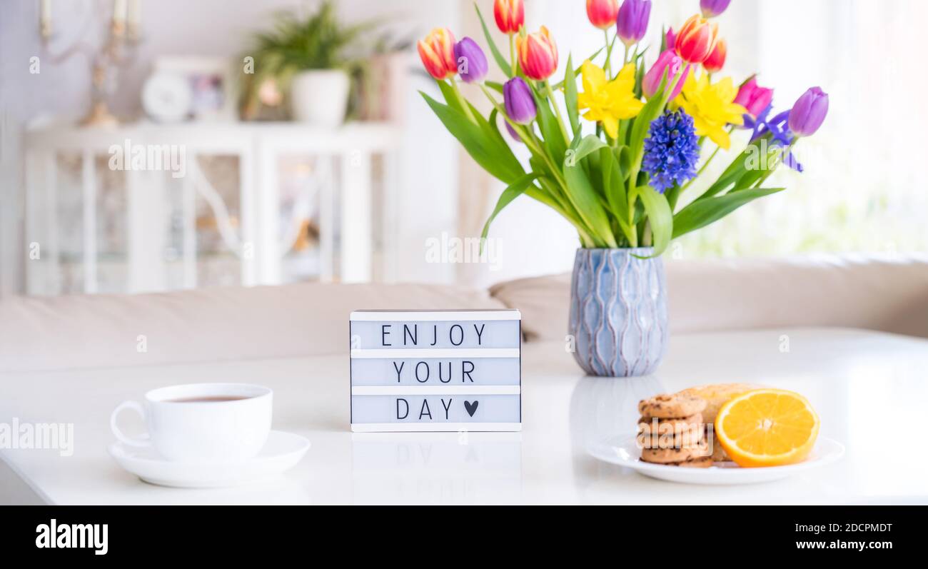 Good Morning Konzept. Romantisches Frühstück - frische Blumen, Tasse Heißgetränk, Kekse, Orange, Leuchtkasten mit Nachricht Genießen Sie Ihren Tag auf Marmortisch mit Stockfoto