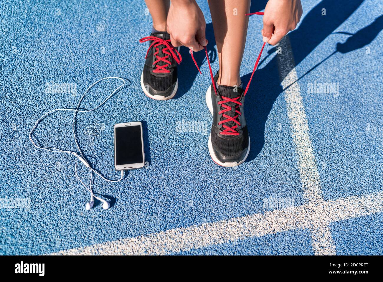 Laufen Motivation Musik auf Handy Läuferin Frau binden Schuh Schnürsenkel. Schuhe und Füße aus der Nähe, Sportler, die sich für Rennen oder Training auf der Laufstrecke vorbereiten Stockfoto