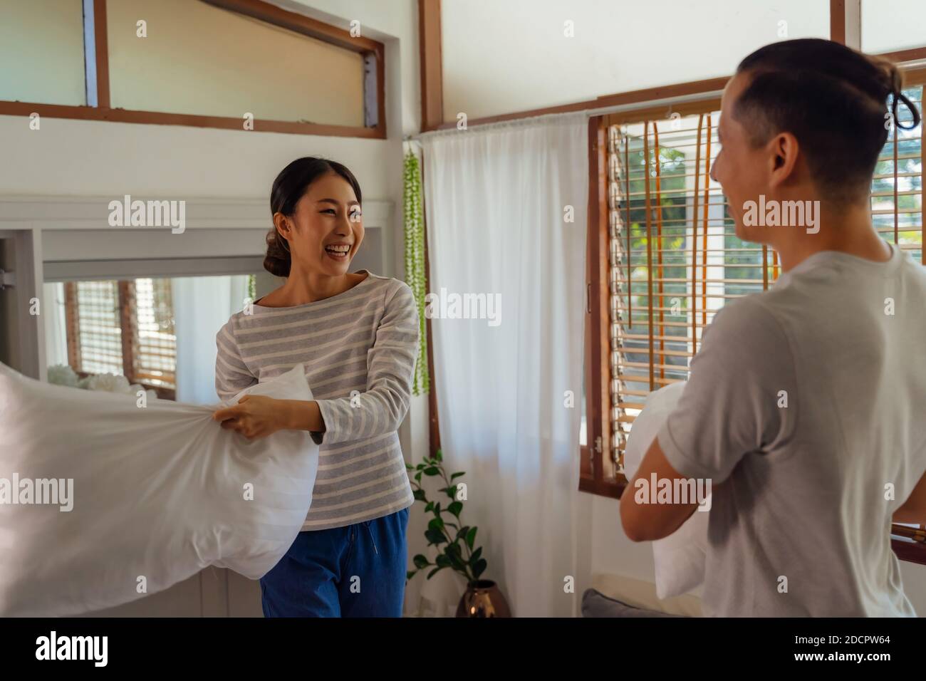 Portrait von jungen erwachsenen asiatischen Paar spielen Kissen Kampf im Schlafzimmer Innenleben Szene. 30s reifen Mann und Frau lächeln und mit einer lustigen Aktivität. Ehe und glückliche Beziehung Leben Konzept Stockfoto