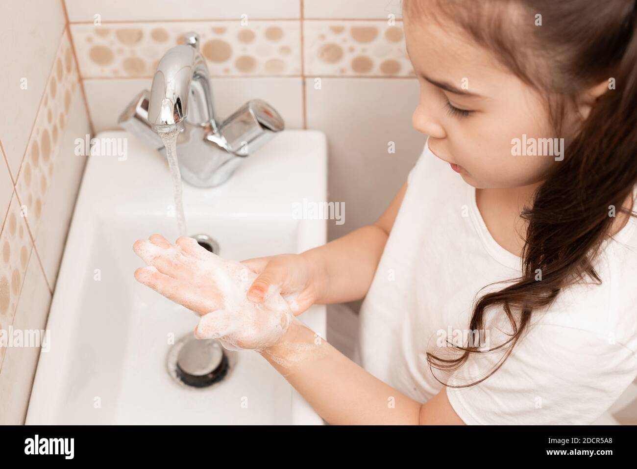 Ein kleines Brünette Mädchen wäscht ihre Handflächen über dem Waschbecken im Badezimmer mit einer Flut von Wasser. Stockfoto