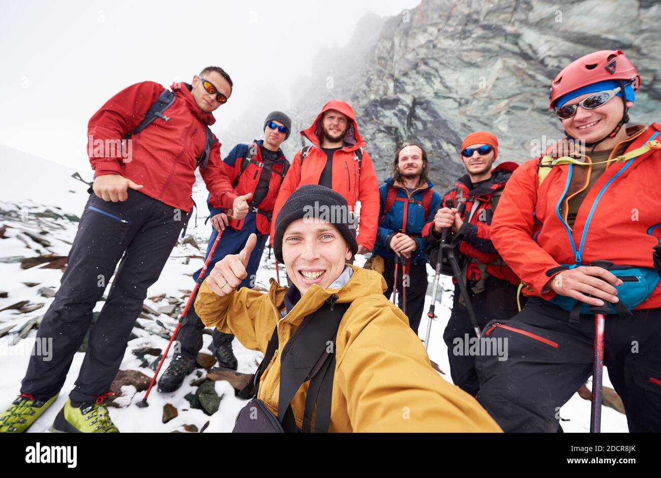 Junger Mann fotografiert mit Freunden Wanderer während der Reise in den Winterbergen. Gruppe von männlichen Reisenden, die die Kamera anschauten und lächelten und Daumen nach oben zeigten. Konzept von Reisen, Wandern und Fotografie. Stockfoto