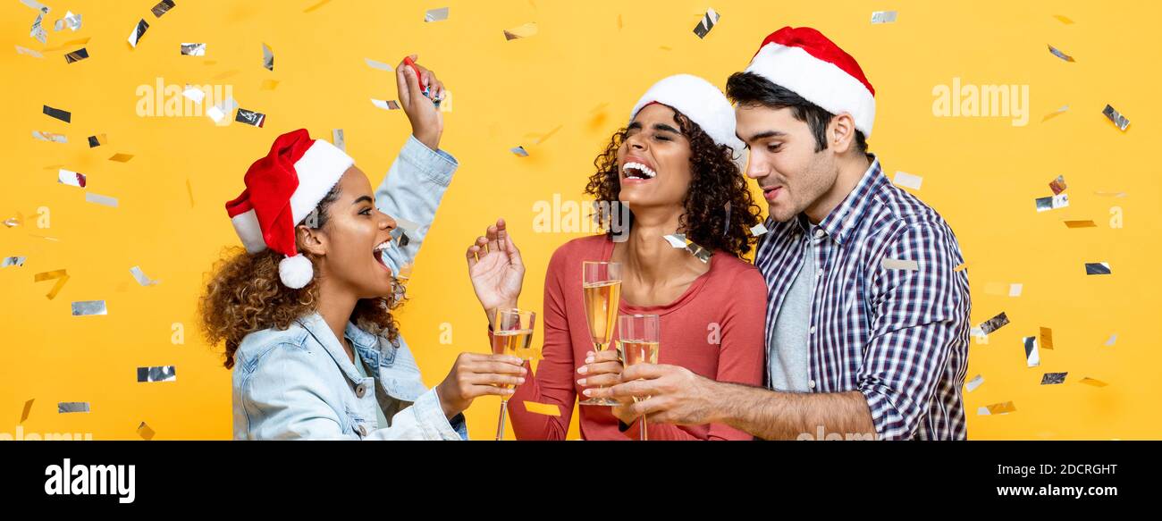 Eine Gruppe von drei glücklichen und vielfältigen Freunden feiert Weihnachten mit Champagner Auf gelbem Studio-Bannrer-Hintergrund Stockfoto