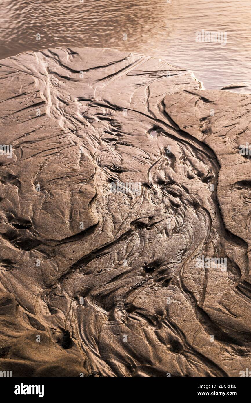 Wasserflecken, die durch eine zurücktretende Flut im Sand hinterlassen werden. Stockfoto