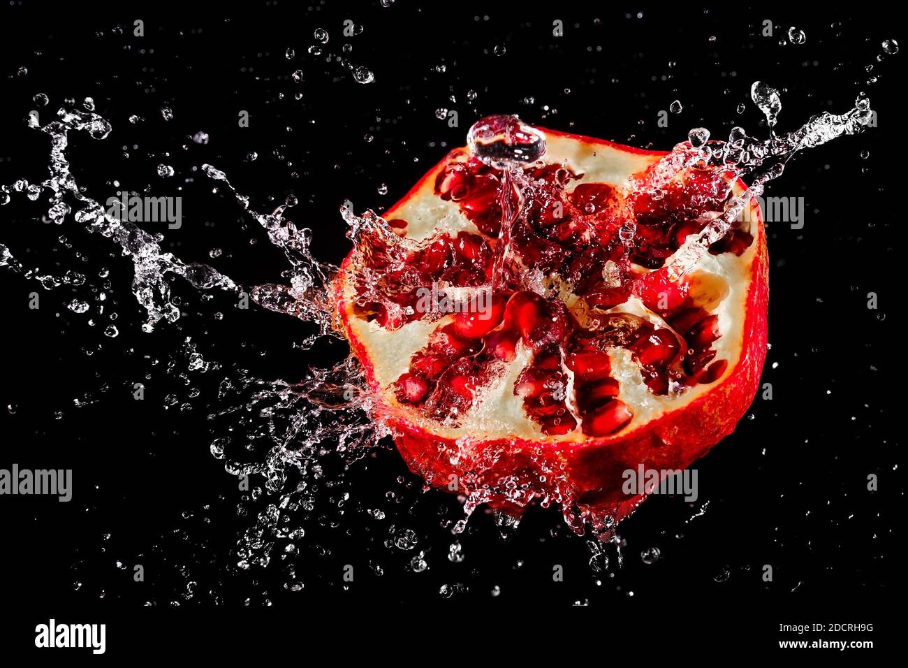 Ein Spritzer Wasser auf einem reifen, saftigen Granatapfel. Dunkler Hintergrund Stockfoto