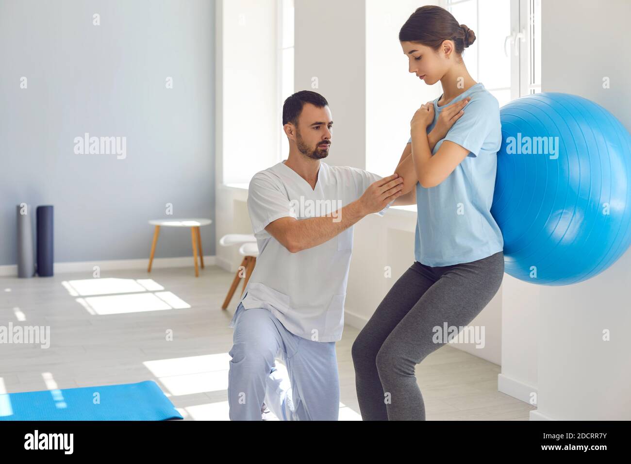 Männliche Physiotherapeutin hilft weiblichen Patienten, Übungen mit Fitness-Ball in Physiotherapie-Raum zu tun. Stockfoto