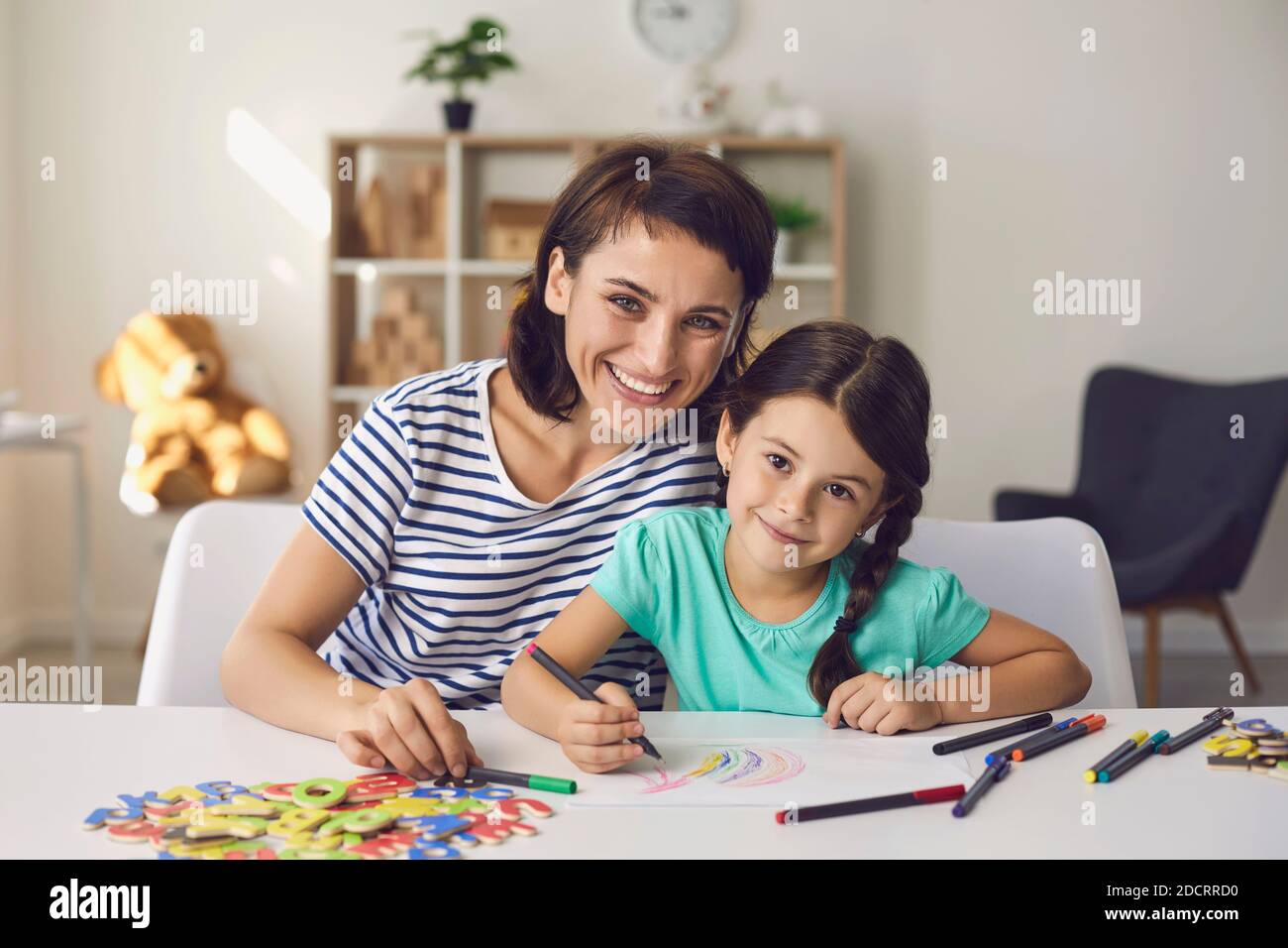 Schöne Mutter und Vorschulmädchen zeichnen mit Filzstiften und lächeln an der Kamera. Stockfoto