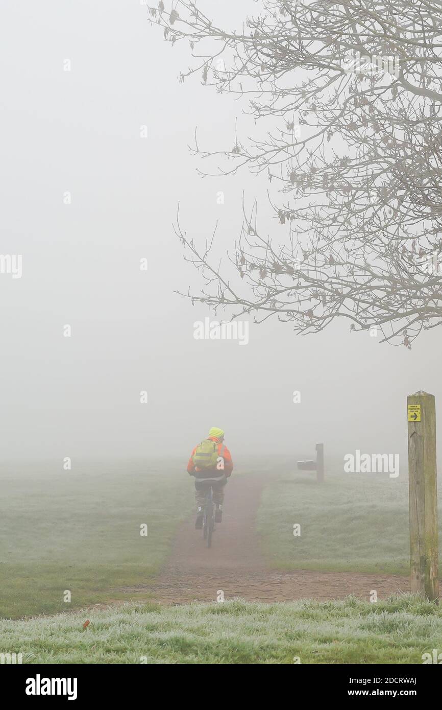 Kidderminster, Großbritannien. November 2020. UK Wetter: Starker Nebel für Pendler in Worcestershire heute. Ein isolierter Radfahrer, der eine Jacke und einen Fahrradhelm trägt, ist hier von hinten zu sehen und fährt an diesem nebligen Morgen durch einen öffentlichen Park auf dem Weg zur Arbeit. Kredit: Lee Hudson/Alamy Live Nachrichten Stockfoto