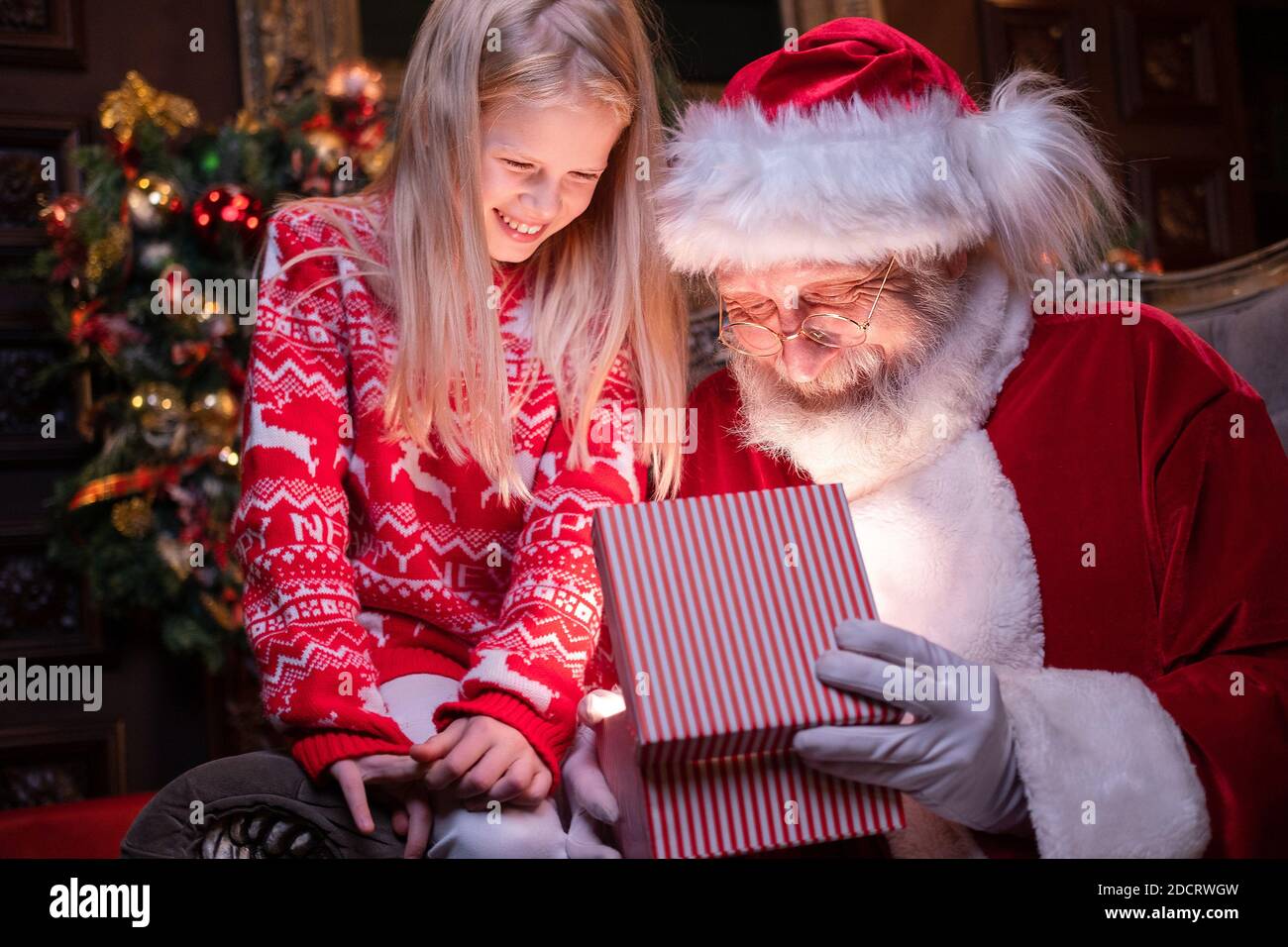 Weihnachtsmann und Mädchen Eröffnung Weihnachtsgeschenk in der Nähe Weihnachtsbaum. Magische Erfüllung der Wünsche Wünsche Stockfoto