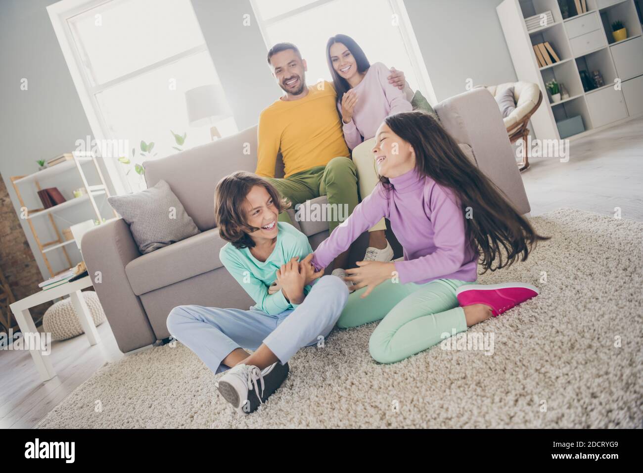 Foto der großen Familie vier Mitglieder sitzen Sofa Teppich Zwei kleine Kinder haben Spaß tragen bunte Pullover Hosen in Wohnzimmer drinnen Stockfoto