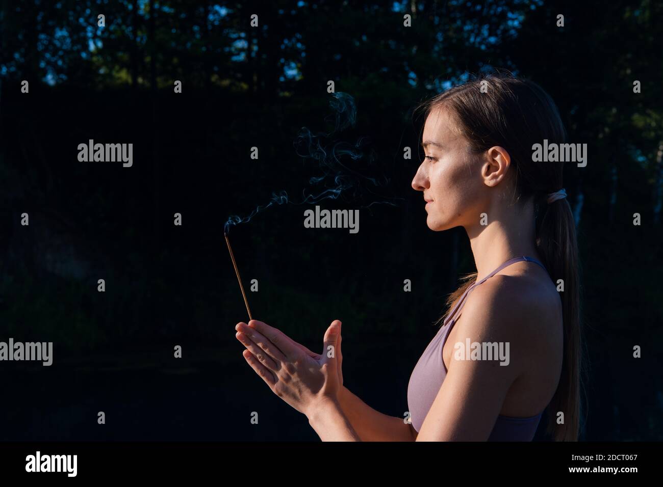 Yoga Frau in Sportkleidung meditieren und atmen auf einem Sonnenaufgang in der Natur. Rauch von aromatischem Stick in den Händen. Stockfoto