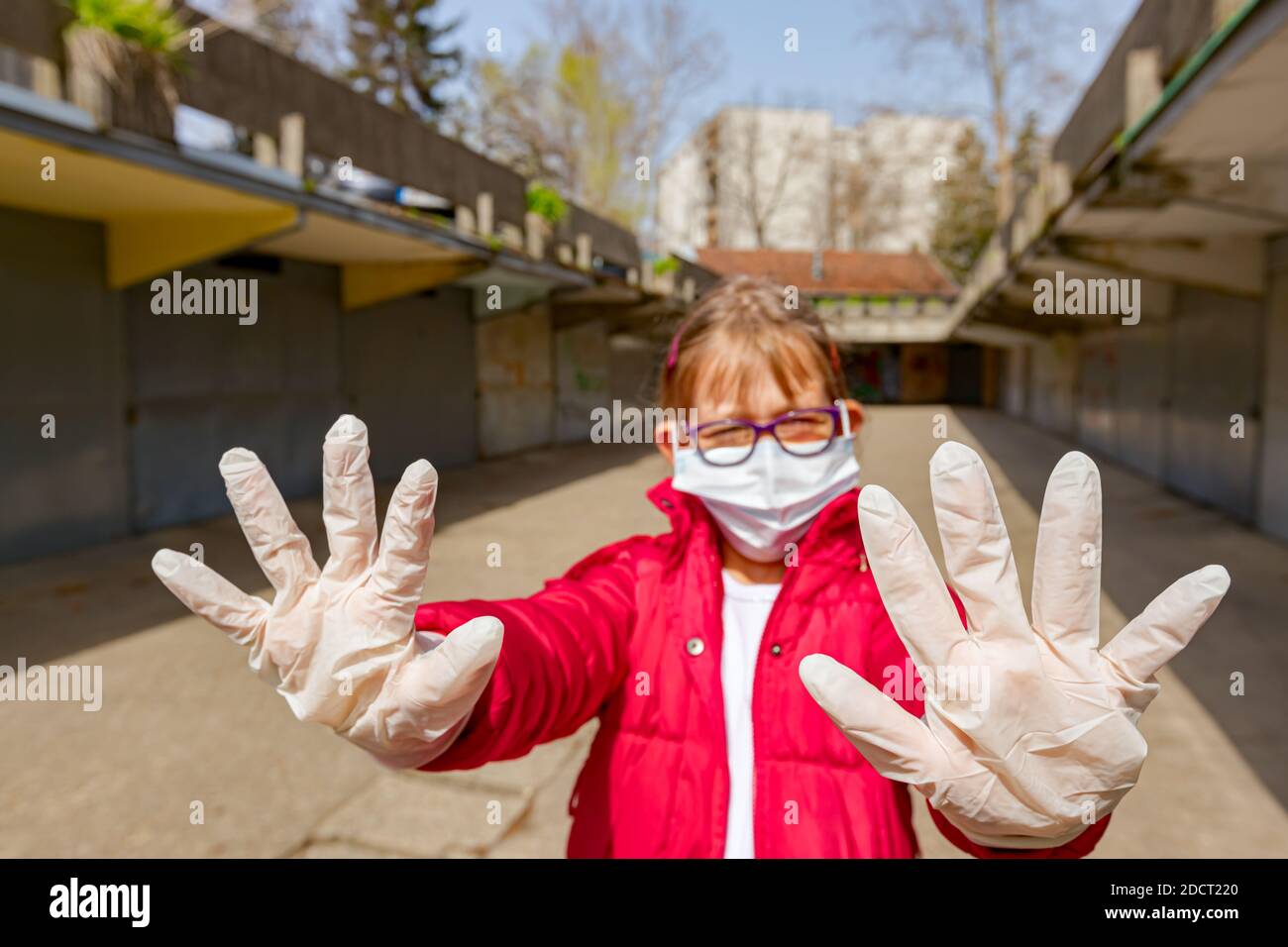 Kleine Mädchen, die medizinische Maske und Handschuhe tragen, halten mit ihren Händen, Gesten, sozialer Distanzierung, bleiben Sie fern, geschützt gegen Virus COVID-19, C Stockfoto