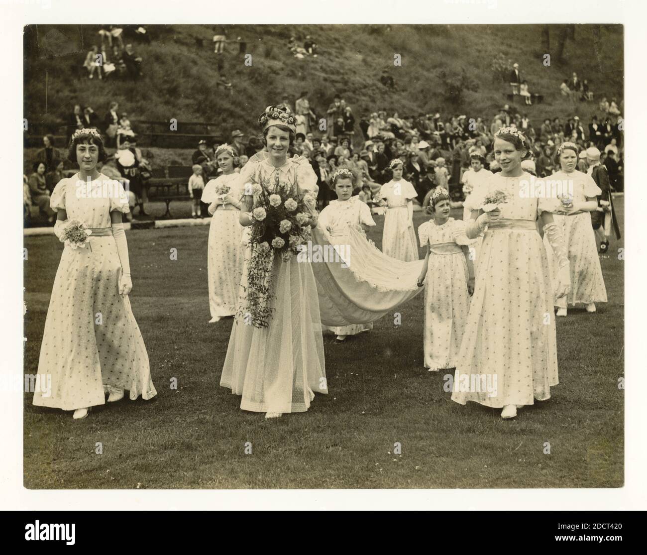 Pressefoto einer großen Menschenmenge aus der Mitte des Jahrhunderts, die die Prozession der frisch gekrönten Rosenkönigin und ihrer Begleiter beobachtet, die den Zug ihres Kleides in einem traditionellen „Walking Day“ in Eagley, Bolton, Lancashire, Nordwestengland, Großbritannien um die 40er Jahre Stockfoto
