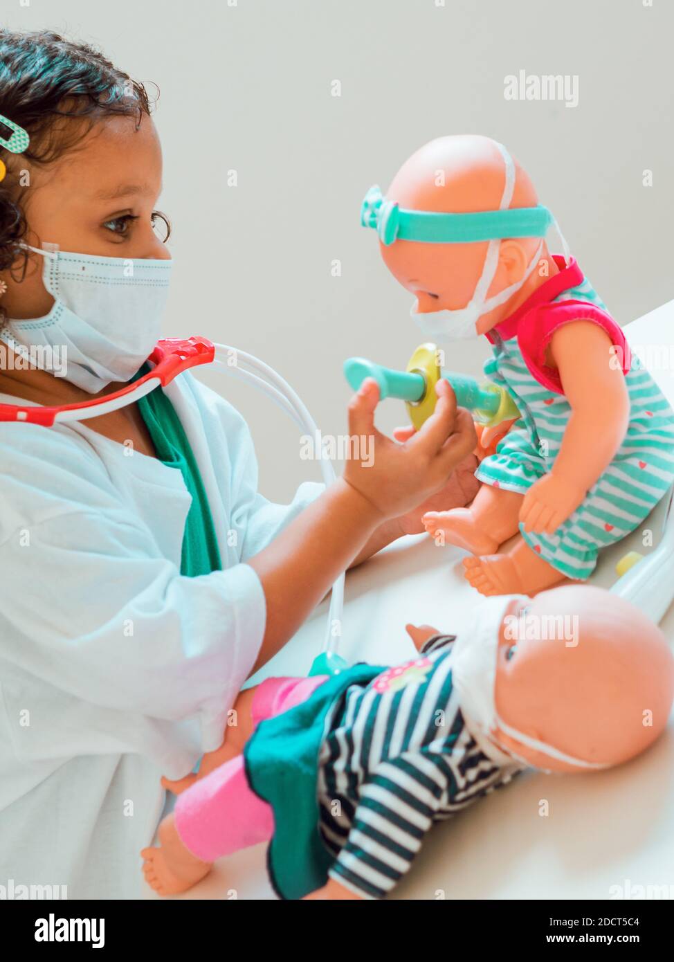 Ein kleines Mädchen, das den Arzt spielt, gibt ihrer Patientin eine Injektion, sie tragen alle Schutzmasken Stockfoto