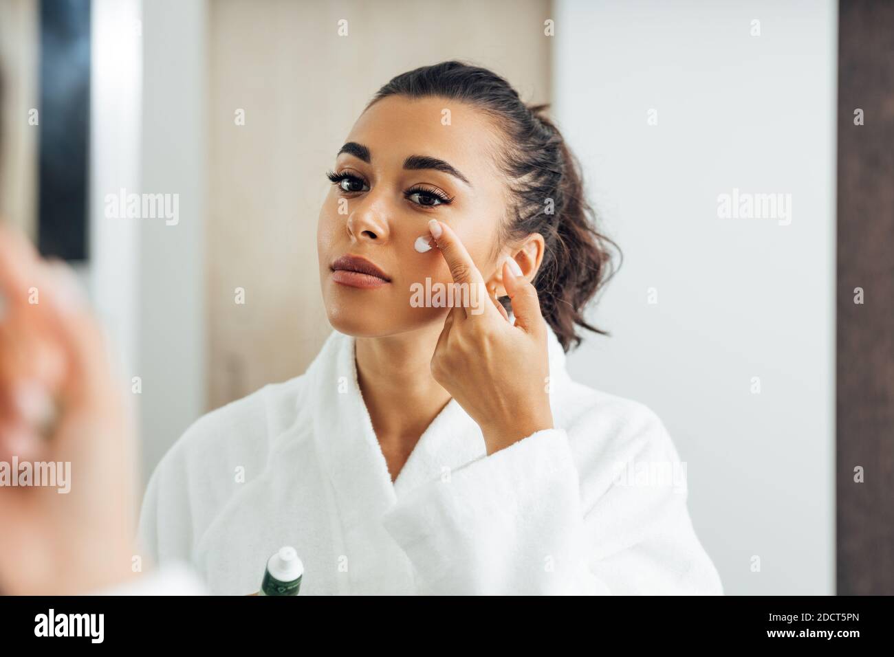 Schöne Frau im Bademantel Anwendung Anti-Aging-Creme auf ihre Wange Stockfoto