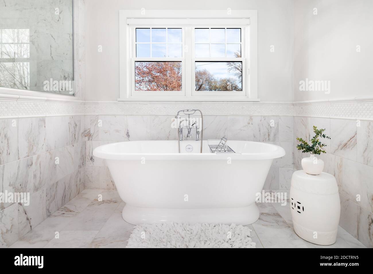 Ein luxuriöses Badezimmer mit einer Victoria + Albert Badewanne und Chrom Wasserhahn umgeben von Marmorfliesen auf dem Boden und an den Wänden. Stockfoto