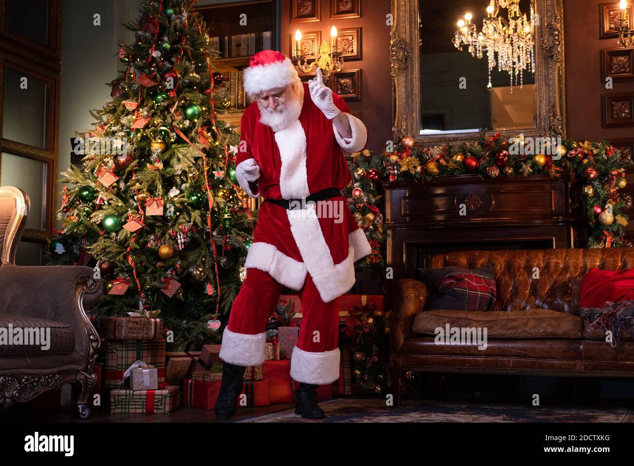 Dancing Santa Vorbereitung Kinder zu gratulieren. Happy Santa Claus Musik hören und tanzen zu Hause in der Nähe des Weihnachtsbaums Stockfoto