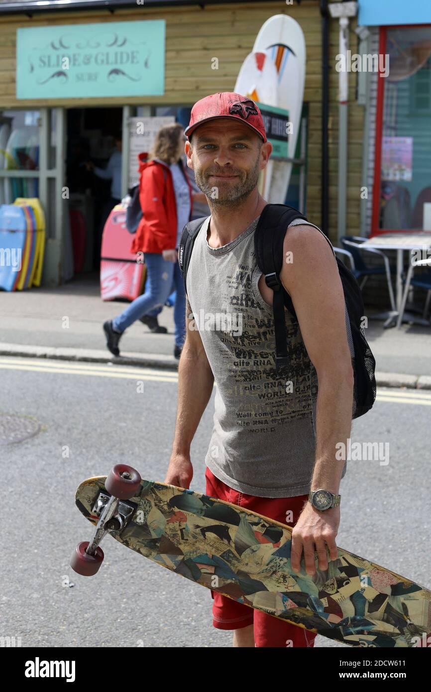 In Newquay, Cornwall, England, hält ein junger Mann sein Skateboard im geschäftigen Stadtzentrum und fängt die lebhafte Atmosphäre dieser beliebten Stadt ein. Stockfoto