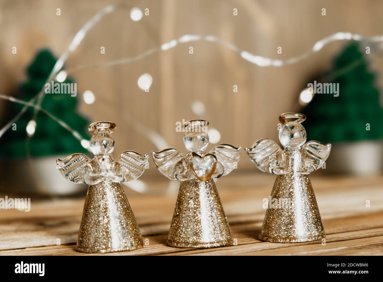Weihnachtskarte mit drei Engeln, Tannenbäumen und einer Girlande auf einem Holzhintergrund.defokussierten Lichter Hintergrund und Weihnachtsdekorationen.Selektiver Fokus Stockfoto