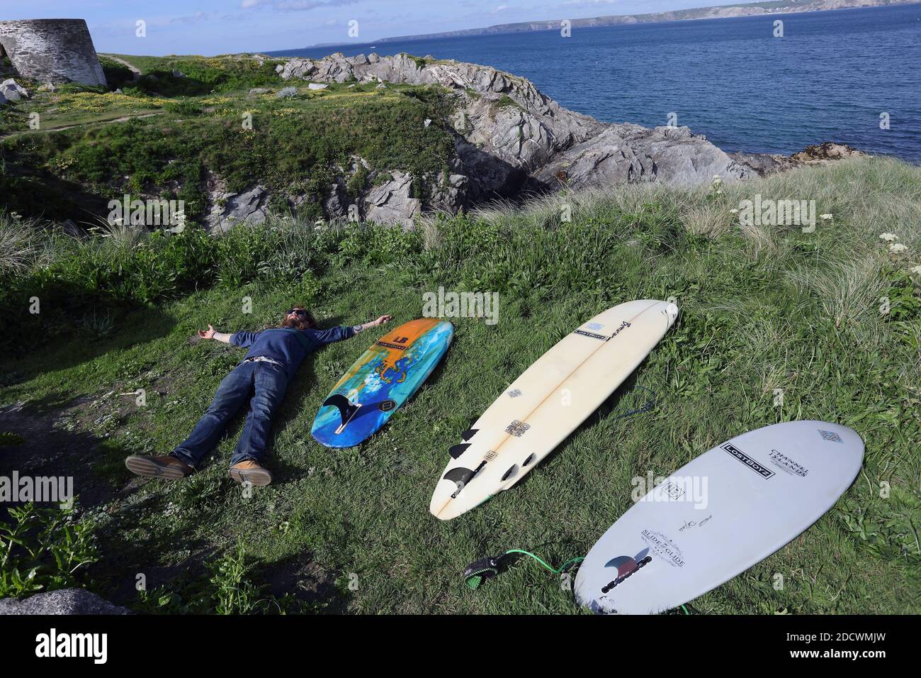 Surfer mit einer Gruppe verschiedener Surfbretter, die auf dem Gras an der zerklüfteten Küste rund um den abgelegenen Little Fistral Beach in Newquay in Cornwall liegen Stockfoto