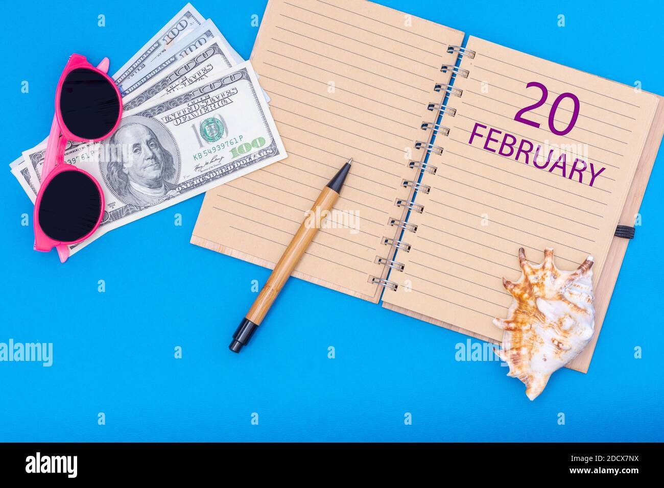 Februar. Tag des 20. Februar. Reiseplan flaches Design mit Notizblock Schreibdatum, Stift, Brille, Gelddollar und Muschel auf blauem Hintergrund. W Stockfoto