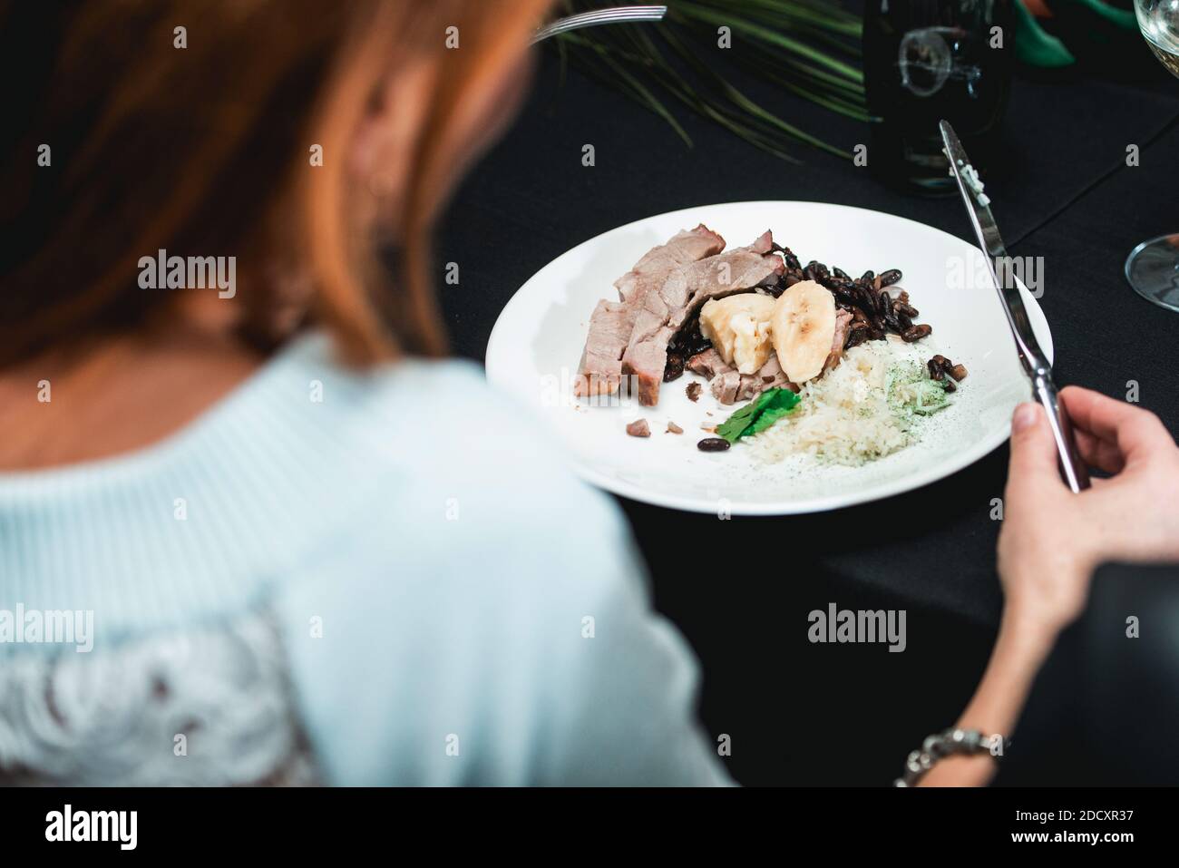 Frau in einem Restaurant essen kubanischen Stil Rindfleisch Picadillo serviert mit weißem Reis und schwarzen Bohnen. Serviert auf einem Tisch mit schwarzer Tischdecke. Stockfoto