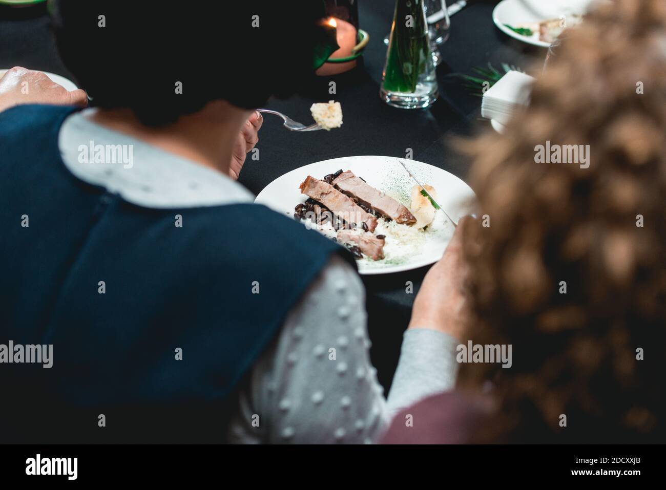 Frau in einem Restaurant essen kubanischen Stil Rindfleisch Picadillo serviert mit weißem Reis und schwarzen Bohnen. Serviert auf einem Tisch mit schwarzer Tischdecke. Stockfoto