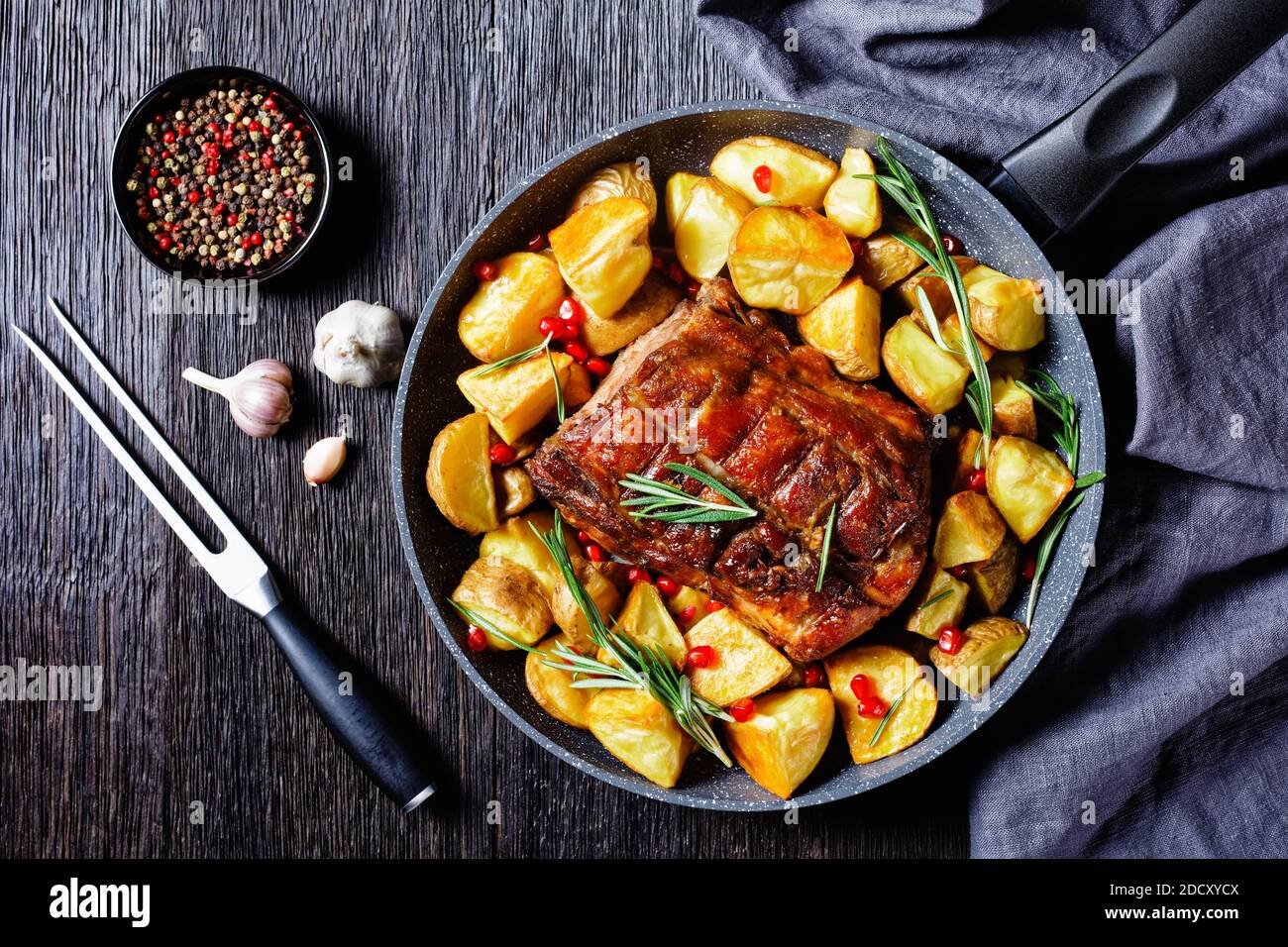 American sunday Braten Dinner: Gebratener Schweinelende mit gebackenen Kartoffelkeilen mit Rosmarin auf einer gusseisernen Pfanne mit Knoblauch und Pfefferkorn auf einem dunklen serviert Stockfoto