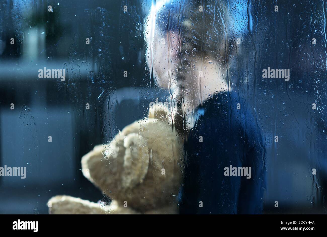 Mädchen mit Teddybär hinter Fenster bedeckt von Regen Drops. Kinder Depression und soziale Fragen konzeptuelles Foto. Stockfoto
