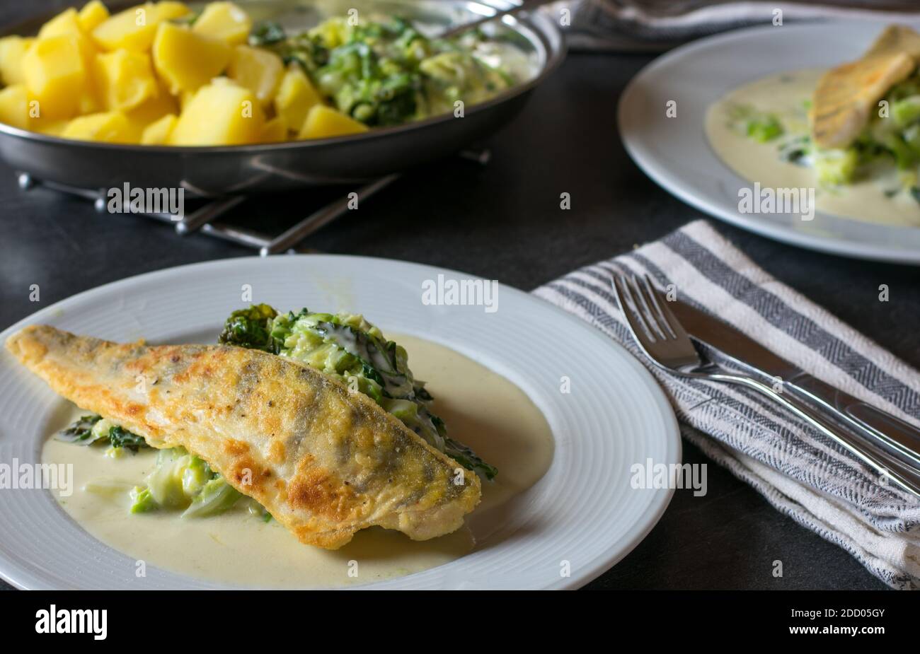 Köstliches Fischgericht mit Hechtbarsch-Filet, savoy-Gemüse, Kartoffeln in einer cremigen Beachamel-Sauce serviert auf einem Küchentisch zu Hause Stockfoto